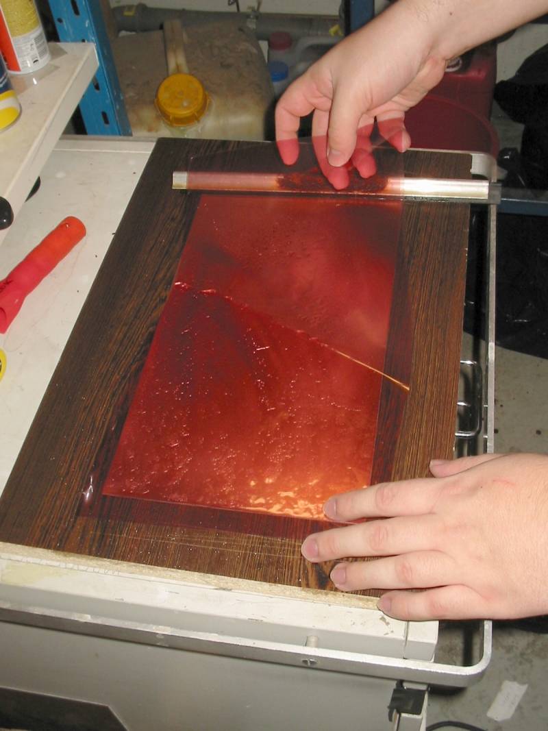 Taikakalvoa asetellaan piirilevyn päälle. Toinen, vielä kiinni oleva suojakalvo jää yläpuolelle, siis ei kuparia vasten. Tässä vaiheessa on tosi mukavaa, jos väliin ei jää kovin suuria pölyhiukkasia, sillä niillä on tapana vaikuttaa kielteisesti lopputulokseen.